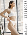 Slim and beautiful woman in white underwear. Young girl with fit body posing in underwear in studio with big windows. Sport, fitness, diet, nutrition and health care concept. 134110938