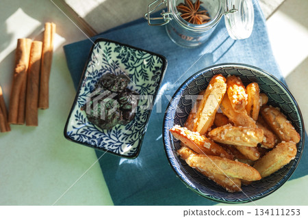 Choux pastry sticks in a ceramic bowl, next to them are cinnamon sticks and dried plums Choux pastry sticks in a ceramic bowl, next to them are cinnamon sticks and dried plums 134111253