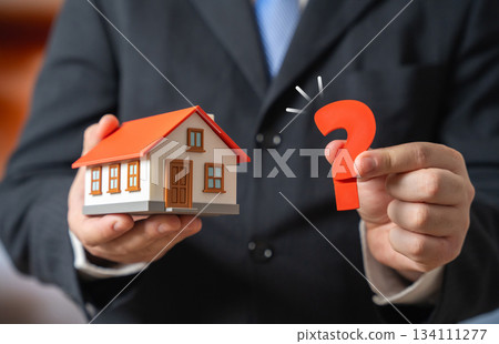 A house and a question mark held by a man in a suit. FAQ on buying and renting a house. Tenant rights. Real estate consulting and support. Housing guides, legal advice and property market. 134111277