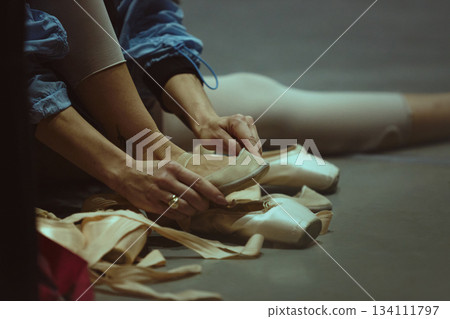 Closeup of hands preparing ballet shoes on studio floor Closeup of hands preparing ballet shoes on studio floor 134111797