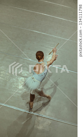 Ballet dancer preparing movement with baton prop on studio floor. Ballet dancer preparing movement with baton prop on studio floor. 134111798