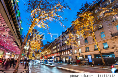Golden Christmas lights illuminate trees along Boulevard Haussmann in Paris, France. Festive holiday decorations brighten the busy street near department stores at night 134112312