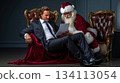 A man in a suit sitting in a chair with a laptop next to a Santa Claus 134113054