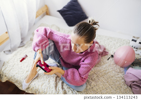 Focused teenage girl handling gaming controller on bed in bedroom 134113243