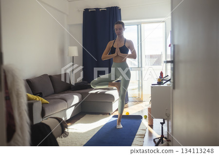 Serene woman maintains tree pose in cozy apartment setting 134113248
