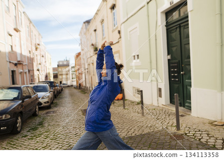 Vibrant figure stretches arms upward amidst pastel buildings Vibrant figure stretches arms upward amidst pastel buildings 134113358