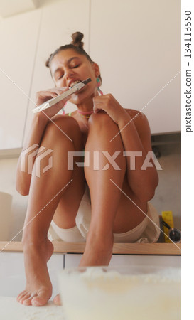 A young girl happily enjoys a tasty snack in a modern, stylish kitchen that feels cozy A young girl happily enjoys a tasty snack in a modern, stylish kitchen that feels cozy 134113550