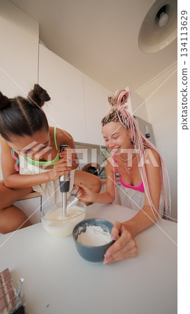Two women joyfully cooking in a bright kitchen, sharing their love for meals and laughter 134113629