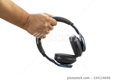 A hand holding black wireless over-ear headphones with cushioned ear pads against a white background in a close-up view. A hand holding black wireless over-ear headphones with cushioned ear pads against a white background in a close-up view. 134114048