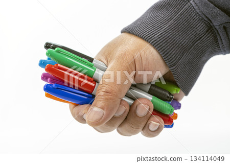 Close-up of a hand tightly holding a collection of colorful permanent markers with various caps visible on a white background 134114049