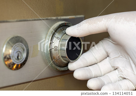Close-up of a gloved hand carefully turning the combination dial on a metal safe lock to ensure security and protection 134114051