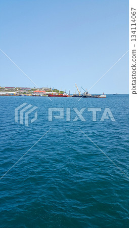 Turquoise Pacific bay with calm, crystalline waters; two ships anchored by a distant island harbor. 134114067
