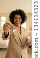 Close-up on house keys with smiling African American woman realtor offering new home, holding documents, inviting client, in modern bright apartment interior. 134114323