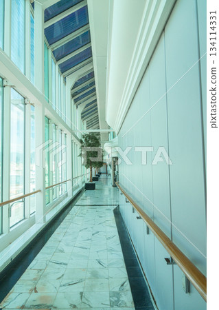 A bright modern corridor with large floor-to-ceiling windows and a glass roof. Marble flooring, clean architectural lines, and soft natural light create an airy, spacious atmosphere suitable for A bright modern corridor with large floor-to-ceiling windows and a glass roof. Marble flooring, clean architectural lines, and soft natural light create an airy, spacious atmosphere suitable for 134114331