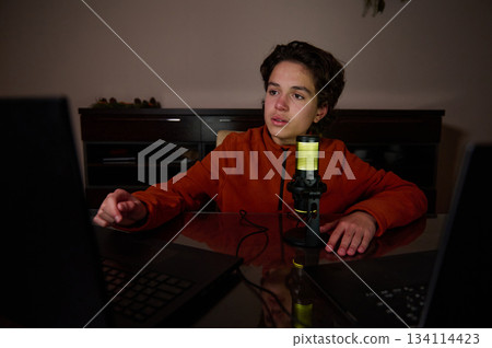 Young Person Recording Podcast At Home Desk With Microphone And Laptop Young Person Recording Podcast At Home Desk With Microphone And Laptop 134114423