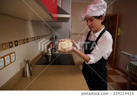 Teen Chef Preparing Pizza in Modern Kitchen Wearing White Hat and Black Apron Teen Chef Preparing Pizza in Modern Kitchen Wearing White Hat and Black Apron 134114428