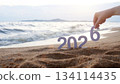 hand place the number 6 on sandy beach, transition from year 2025 to 2026 for new year sign on summer beach at sunset time, with ripple sea wave and beautiful nature at background, New Year celebrate 134114435