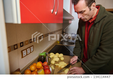 Man Chops Potatoes In A Modern Kitchen For Meal Preparation Man Chops Potatoes In A Modern Kitchen For Meal Preparation 134114447