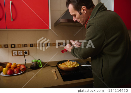 Man Cooking Potatoes On Stove In Modern Kitchen With Red Cabinets Man Cooking Potatoes On Stove In Modern Kitchen With Red Cabinets 134114450