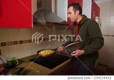 Man Cooking Potatoes In Frying Pan On Kitchen Stove With Lid 134114451
