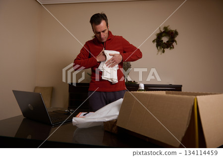 Man Unpacking Holiday Packages At Home With Laptop And Cardboard Box 134114459