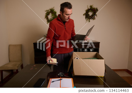 Man In Red Sweater Packing Box With Laptop At Home For Christmas Setup Man In Red Sweater Packing Box With Laptop At Home For Christmas Setup 134114463