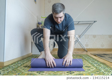 Plus-size man practicing yoga at home on a mat, stretching to improve flexibility, joint mobility and posture. Concept of home fitness, rehabilitation, wellness and mindful movement. 134115214