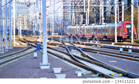 Warsaw, Poland. 28 November 2025. A passenger train on the tracks near the station. Tracks, electrical wires and metal masts against the backdrop of a city skyscrapers on a winter day.  134115221