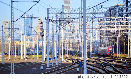 Warsaw, Poland. 28 November 2025. A passenger train on the tracks near the station. Tracks, electrical wires and metal masts against the backdrop of a city skyscrapers on a winter day.  134115222