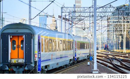 Warsaw, Poland. 28 November 2025. A passenger train on the tracks near the station. Tracks, electrical wires and metal masts against the backdrop of a city skyscrapers on a winter day. Warsaw, Poland. 28 November 2025. A passenger train on the tracks near the station. Tracks, electrical wires and metal masts against the backdrop of a city skyscrapers on a winter day. 134115225