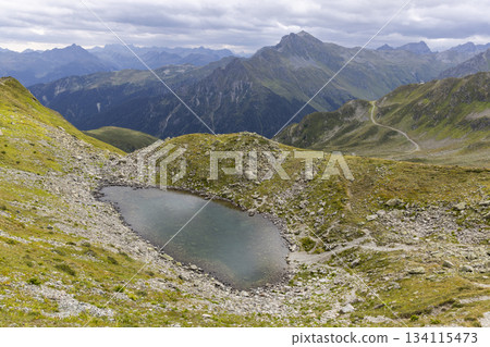 Hikers explore Smugglerpfad trail in Gargellen, Montafon, Vorarlberg, Austria with scenic mountains and a small lake Hikers explore Smugglerpfad trail in Gargellen, Montafon, Vorarlberg, Austria with scenic mountains and a small lake 134115473