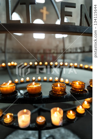 Burning votive candles warm glow in circular stand rack at French catholic cathedral church dark background. Prayer, hope, faith, remembrance prayer spirit in tranquil atmosphere Burning votive candles warm glow in circular stand rack at French catholic cathedral church dark background. Prayer, hope, faith, remembrance prayer spirit in tranquil atmosphere 134115644
