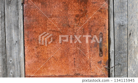 Rusty metal door with simple handle in the structure of a wooden building made of gray aged boards as a peasant style background, barn or shed door made of oxidized iron Rusty metal door with simple handle in the structure of a wooden building made of gray aged boards as a peasant style background, barn or shed door made of oxidized iron 134115945