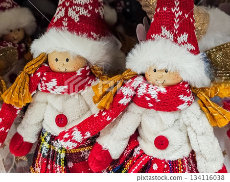 Close-up of two girl figurines wearing red hats, red scarves, and white winter coats. Holiday-themed decorative dolls captured in soft lighting. Close-up of two girl figurines wearing red hats, red scarves, and white winter coats. Holiday-themed decorative dolls captured in soft lighting. 134116038