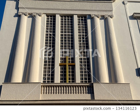 Church facade with tall columns and golden cross under clear sky. Religious heritage, spiritual architecture, solemn atmosphere and timeless cultural significance. Church facade with tall columns and golden cross under clear sky. Religious heritage, spiritual architecture, solemn atmosphere and timeless cultural significance. 134116123