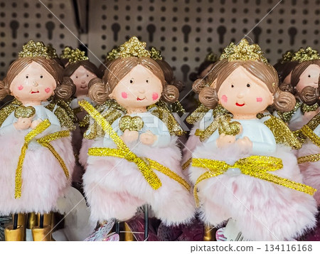 Close-up of whimsical princess figurines wearing light-colored dresses with semi-transparent skirts and crowns, each holding a small golden heart. Decorative figurines suitable for holiday displays 134116168