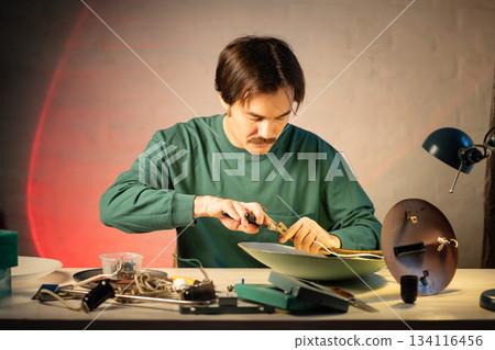 Man crafter enjoying upcycling hobby, restoring and repairing old used vintage lamp at workshop. 134116456