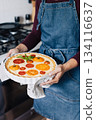 Female hands holding cheese and tomato quiche in the ceramic baking dish. 134116637