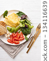 French omelet, avocado, tomatoes, salad, cheese, and bread toast on plate. Healthy breakfast on white table, angle view. 134116639