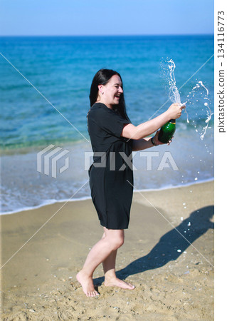 Happy woman opening sparkling wine bottle on beach celebrating success Happy woman opening sparkling wine bottle on beach celebrating success 134116773