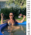 Woman relaxing in inflatable pool making hand gestures in garden 134116811