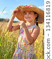 Smiling girl holding straw hat standing in wheat field on sunny summer day 134116819
