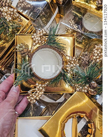 A golden candle holder decorated with evergreen sprigs and holiday ornaments being gently held at hand level. The scene features warm festive details, emphasizing Christmas decor, seasonal ambiance 134117020