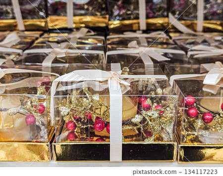 Photo of a row of festive gift boxes accompanied by gold and red Christmas candle holders. The composition highlights traditional holiday colors, seasonal decorations, and cozy festive ambiance Photo of a row of festive gift boxes accompanied by gold and red Christmas candle holders. The composition highlights traditional holiday colors, seasonal decorations, and cozy festive ambiance 134117223