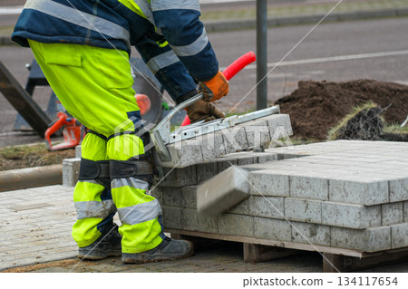 Road worker lifting concrete paving blocks with tool during construction of sidewalk on urban street Road worker lifting concrete paving blocks with tool during construction of sidewalk on urban street 134117654