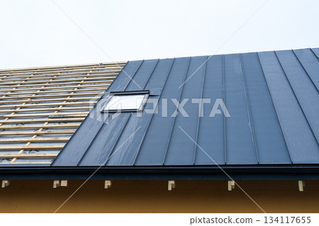 Modern metal roof installation with skylight on residential house under construction 134117655
