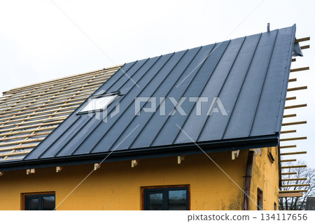 Modern house roof renovation with black metal panels and skylight during construction process 134117656