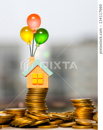Tiny house with colorful balloons standing on a stack of gold coins symbolizing dream home savings 134117660