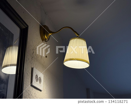 Wall lamp glowing in cafe corner. Interior lighting, evening ambiance, decor detail and warm relaxation atmosphere Wall lamp glowing in cafe corner. Interior lighting, evening ambiance, decor detail and warm relaxation atmosphere 134118271