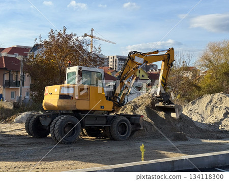 Yellow excavator moving soil. Heavy machinery, construction work and industrial progress in urban environment. 134118300